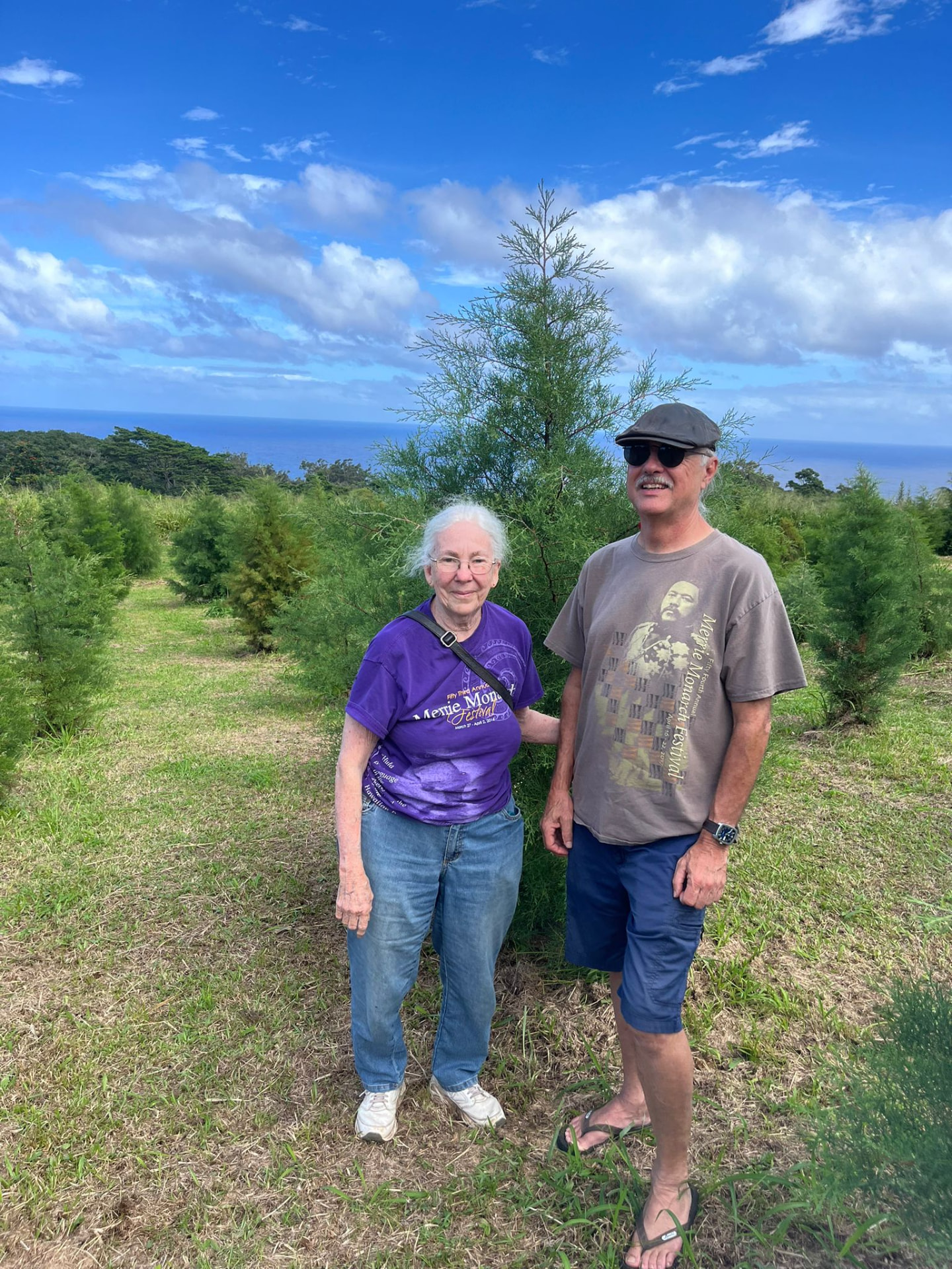 Couple standing beside their Christmas tree overlooking the Pacific Ocean at Hamakua Christmas Tree Forest